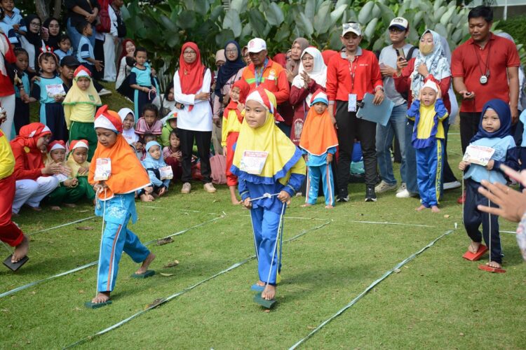 Foto seorang anak perempuan di lapangan rumput sedang berlomba permainan bakiak tali atau egrang balok